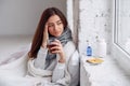 Woman feels a headache and holds her hand to her head. Close up of beautiful young woman in warm plaid with hot cup of