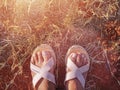 The woman feet with sandals standing on the on the dry grass field and the red clay soil