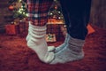 Woman feet standing in tip toe in winter socks on male lags on a fluffy red blanket near a Christmas tree with gifts. Concept. Royalty Free Stock Photo