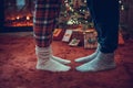 Woman feet standing in tip toe in winter socks on male lags on a fluffy red blanket near a Christmas tree with gifts. Concept. Royalty Free Stock Photo