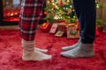 Woman feet standing in tip toe in winter socks on male lags on a fluffy red blanket near a Christmas tree with gifts. Concept. Royalty Free Stock Photo