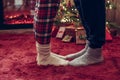 Woman feet standing in tip toe in winter socks on male lags on a fluffy red blanket near a Christmas tree with gifts. Concept. Royalty Free Stock Photo