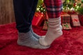 Woman feet standing in tip toe in winter socks on male lags on a fluffy red blanket near a Christmas tree with gifts. Concept. Royalty Free Stock Photo