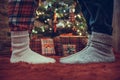 Woman feet standing in tip toe in winter socks on male lags on a fluffy red blanket near a Christmas tree with gifts. Concept. Royalty Free Stock Photo