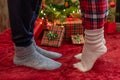 Woman feet standing in tip toe in winter socks near male lags on a fluffy red blanket near a Christmas tree with gifts. Concept. Royalty Free Stock Photo