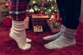 Woman feet standing in tip toe in winter socks near male lags on a fluffy red blanket near a Christmas tree with gifts. Concept. Royalty Free Stock Photo