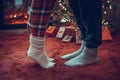 Woman feet standing in tip toe in winter socks near male lags on a fluffy red blanket near a Christmas tree with gifts. Concept. Royalty Free Stock Photo