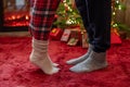 Woman feet standing in tip toe in winter socks near male lags on a fluffy red blanket near a Christmas tree with gifts. Concept. Royalty Free Stock Photo