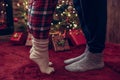 Woman feet standing in tip toe in winter socks near male lags on a fluffy red blanket near a Christmas tree with gifts. Concept. Royalty Free Stock Photo