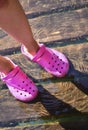 Woman feet in transparent water with crox rubber slippers on wooden pier