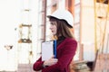 Female architect or engineer holding blueprint and wearing white safety helmet on building construction background. Royalty Free Stock Photo