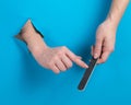 Woman filing her nails through a hole on a blue background. Royalty Free Stock Photo