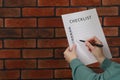 Woman filling Checklist against brick wall, closeup. Space for text