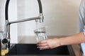 Woman filling drinking glass with tap water on the kitchen. Concept of clean drinking tap water at home. Pouring fresh