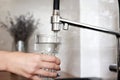 Woman filling drinking glass with tap water on the kitchen. Concept of clean drinking tap water at home. Pouring fresh Royalty Free Stock Photo