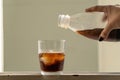 Woman is filling a glass cup with ice cubes with cola