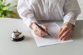 Woman filling hotel reservation form. Silver vintage bell on reception desk. Hotel service, registration. Royalty Free Stock Photo