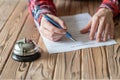 Woman filling hotel reservation form on wooden rustic reception desk with silver vintage bell. Hotel service, registration. Royalty Free Stock Photo