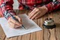 Woman filling hotel reservation form on wooden rustic reception desk with silver vintage bell. Hotel service, registration. Royalty Free Stock Photo