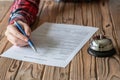 Woman filling hotel reservation form on wooden rustic reception desk with silver vintage bell. Hotel service, registration. Royalty Free Stock Photo