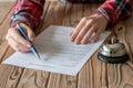 Woman filling hotel reservation form on wooden rustic reception desk with silver vintage bell. Hotel service, registration. Royalty Free Stock Photo