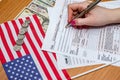 Woman fills the tax form 1040 with money, pen, flag of USA and calculator