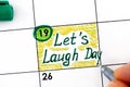 Woman fingers with pen writing reminder Lets Laugh Day in calendar