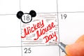 Woman fingers with pen writing reminder Mickey Mouse Day in calendar