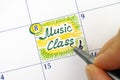 Woman fingers with pen writing reminder Music Class in calendar