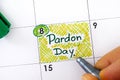 Woman fingers with pen writing reminder Pardon Day in calendar