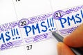 Woman fingers with pen writing reminder PMS in calendar.