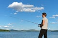 Woman fisherman catches a fish from a blue lake against a blue sky with clouds. Bright shot