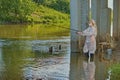 woman fisherman catches fish under a bridge in a river in a protective suit and mask. concept. virus. ecology.