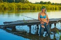 Woman fisherman in a swimsuit catches fish with a fishing rod at the pier from the shore