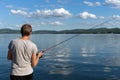 Woman is fishing from a beautiful blue lake against a mountainous shore and the sky with clouds. Bright shot