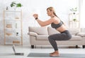 Woman with fitness tracker crouches and watches at laptop in living room interior Royalty Free Stock Photo