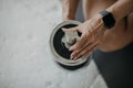 Woman with fitness tracker sits on floor and adjusts weight of dumbbell for hand exercises at gym