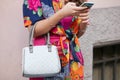 Woman with floral dress and gray bag looking at smartphone before Giorgio Armani fashion show,