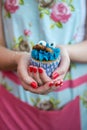 Woman in Floral dress with painted nails holding blue cupcake