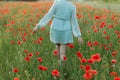 Woman in floral dress walking in poppy field in evening summer countryside. Atmospheric moment. Young female relaxing and Royalty Free Stock Photo