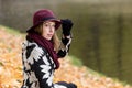 Woman in a floral patterned coat and wine red hat in the park, by the river. Happy girl, colorful autumn forest. Portrait of lady