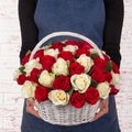 Woman florist in blue apron holding fresh bouquet of red and white flowers in basket against light brick wall background Royalty Free Stock Photo