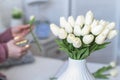 Woman florist cutting stem of tulips flowers with scissors and putting in vase on coffee table. Composing bouque.