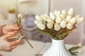 Woman florist cutting stem of tulips flowers with scissors and putting in vase on coffee table. Composing bouque.