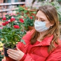 Woman florist in face mask chooses red roses flowers in shop. Buying indoor plants for home gardening with coronavirus quarantine Royalty Free Stock Photo