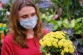 Woman florist in face mask chooses yellow chrysanthemum flowers in shop. Growing flowers and plants at home during corona virus Royalty Free Stock Photo