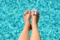 Woman with flower holding feet over water in swimming pool, closeup Royalty Free Stock Photo