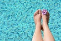 Woman with flower holding feet over water in swimming pool, closeup. Space for text Royalty Free Stock Photo
