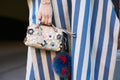 Woman with flowers decorated bag, Cartier Clou golden bracelet and white and blue striped dress before Fendi