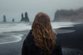 Woman flowing hair stands facing stormy seas rock formations black sand beach Royalty Free Stock Photo